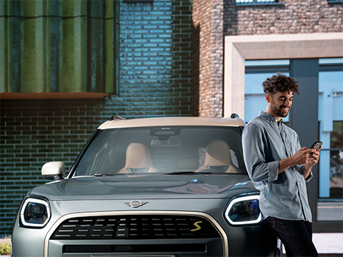 Vediamo un ragazzo che guarda lo smartphone appoggiato di schiena alla sua MINI.